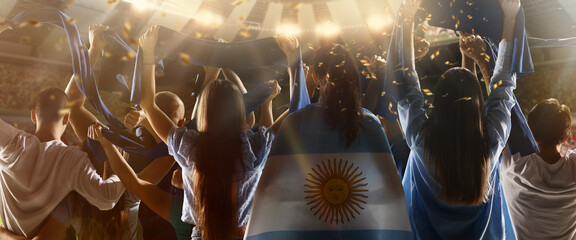 Back view of football, soccer fans from Argentina cheering their team with blue-white state flags and scarfs at crowded stadium.