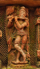 Fototapeta na wymiar Carving sculpture of Lord Krishna on the Sukasari Temple, Bhubaneswar, Odisha, India. Built in sandstone with carvings of human figures, deities, scroll work and floral motifs on walls.