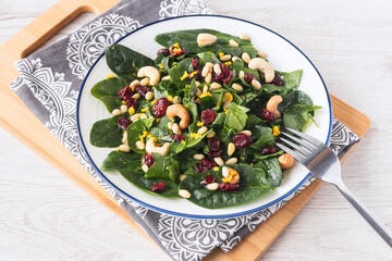On a white plate, fresh vitamin salad with spinach leaves, cashews, pine nuts, dried cranberries,...