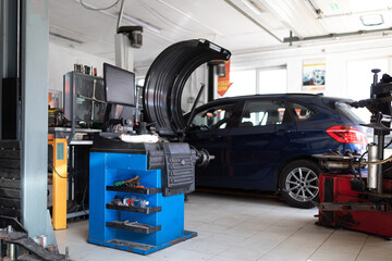 Photo of a machine for balancing wheels and repairing tires of an auto against the background of a blue passenger car at a service station at a repair with an open hood