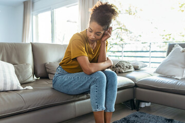 Worried mature woman waiting for news with her smartphone while sitting on couch at home.