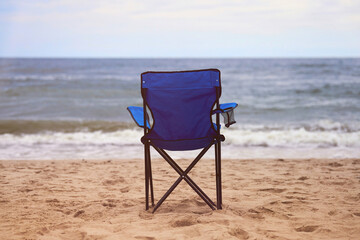 Blue folding chair back on sea beach, without people, beach holiday alone, loneliness