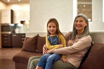 Caring nanny and lovely girl sitting on sofa