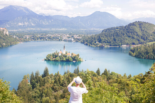 torist takes a pickture of the castle in the middle of a clean mountainous emerald lake Bled against the backdrop of the Slovenian Alps