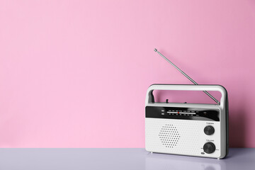 Retro radio receiver on table against pink background. Space for text