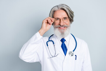 Photo of cheerful positive senior man doc dressed white uniform arm spectacles smiling isolated grey color background