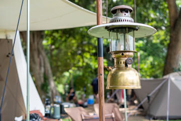 Close up Beautiful vintage camping brass lantern hanging on a wooden stand with a background of tents in the camping,Relaxing in the midst of nature