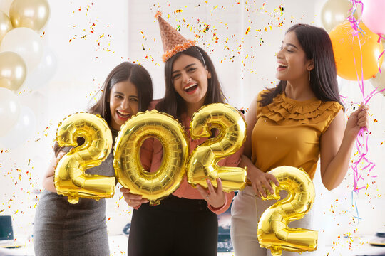 Friends partying together in office holding 2022 balloons. 	