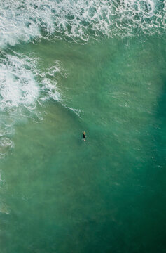 Aerial view of a person with surfboard in the ocean along the coastline near St Agnes, Cornwall, United Kingdom.