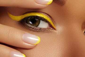 Close-up Female Eye with bright yellow Eyeliner Makeup. Neon Disco make-up and Fashion Manicure. Summer beauty style