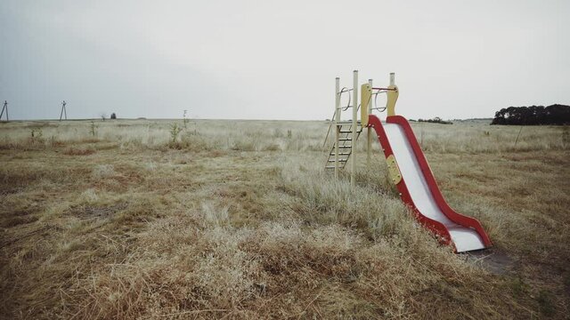 Сhildren's slide in a deserted place. Dried grass field. Empty playground in the countryside. Sunny day.