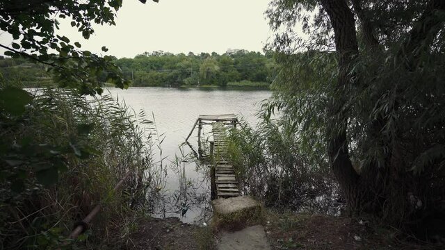 Water landscape. An abandoned wooden pier is surrounded by reeds. Fishermen's bank by the river. Quiet secluded place by the lake.