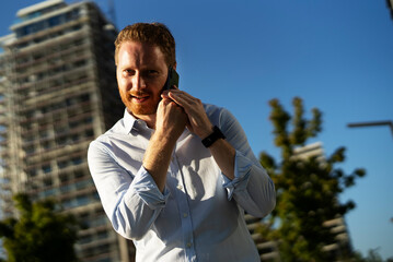 Young happy businessman outdoors. Portrait of handsome man talking to the phone.