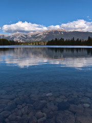Beautiful view of Lake Beauvert in Jasper, Alberta, Canada with reflections in the calm water and round stones below the surface on sunny day in autum.