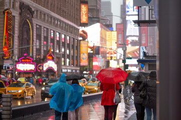 Some people are walking in Times Square during a rainy day. Times Square is a major commercial intersection, tourist destination in Midtown Manhattan.