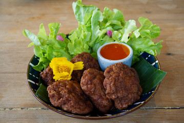 Selective focus of fried porks in the blue plate decorated with banana leaf, green vegetable and yellow flower, and sauces.  Fried porks plate on wood table in natural light.