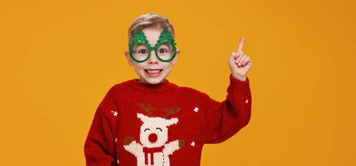 Smiling little boy wearing funny glasses in form of Christmas trees pointing with finger upside