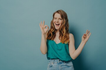 Charming funny girl shows OK sign with hands, winking and looking at camera with big smile