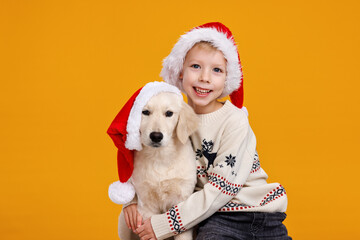 Charming christmas portrait of little boy and Golden Retriever puppy wearing Santa hats