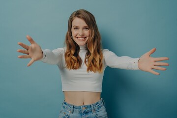 Young happy positive female in casual clothes spreading her arms wide in desire to welcome someone