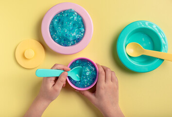 Child playing with blue slime and kitchen set toy on yellow background. Educational, sensory and role play for kids. top view
