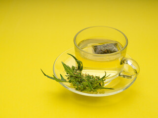 Cannabis tea in a teacup and marijuana buds flower isolated on a yellow background