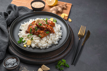 Teriyaki chicken with rice and sesame seeds in a black plate.