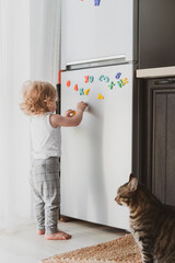 little cute toddler playing with toy letters on the fridge