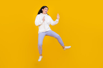 Fototapeta na wymiar Photo of pretty sportive lady jump kick air have fun wear white hoodie isolated yellow color background