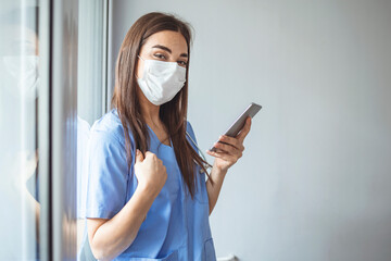 Shot of a masked young doctor using a smartphone. Sad modern physician woman using phone app. Female nurse using smartphone on her way to work. Taking break, nurse talks on smart phone