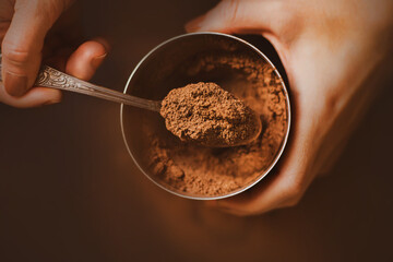 A woman with a brown manicure on her nails holds a jar of fragrant crumbly cocoa powder in her...