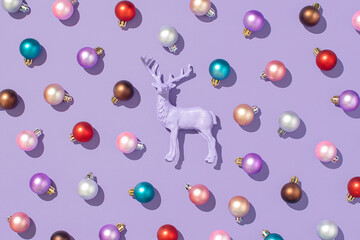 Christmas pattern made of colorful bauble and purple reindeer on a purple background. New Year flat lay concept.