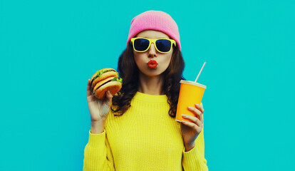 Portrait of stylish young woman with burger and cup of juice fast food on blue colorful background