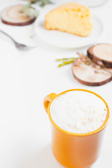 Latte, cinnamon, piece of orange cake, wooden coaster and dry leaves and flowers on beige background. Fall, autumn concept.