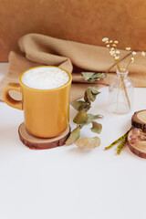 Latte, cinnamon, wooden coaster and dry leaves and flowers on beige background. Fall, autumn concept.