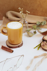Latte, cinnamon, wooden coaster and dry leaves and flowers on beige background. Fall, autumn concept.