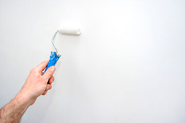 Man's hand painting the wall with a roller. Place for your text. Repair