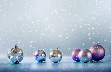 Purple and silver Christmas tree bulbs on blue background with falling snow