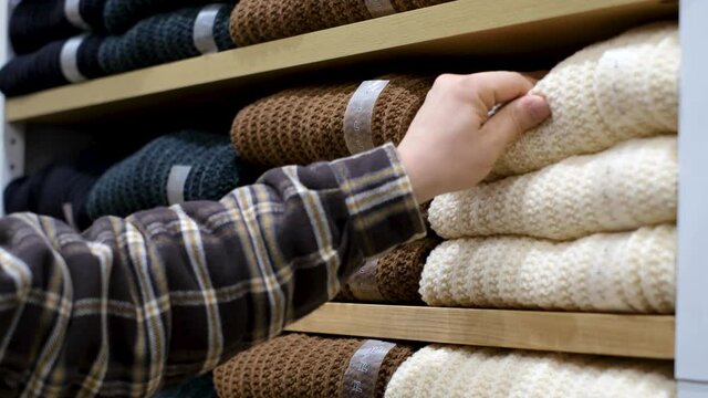 Man chooses jersey sweaters lying on shelves in the store.