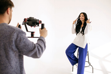 A young woman blogger shoots a video blog in the studio with the help of a videographer with a...