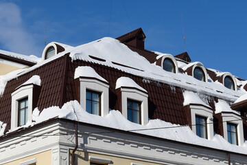 Winter buildings against the blue sky. Long icicles hanging from roofs and eaves, dangerous for people's lives.