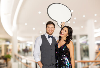 fashion, style and sale concept - happy couple hugging at party and holding blank text bubble...