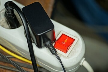 part of a white electrical extension cord with a red button and sockets with a black charger and...