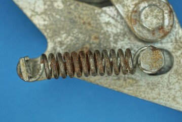 one old iron brown rusty spring on a gray metal structure with a bolt on a blue table