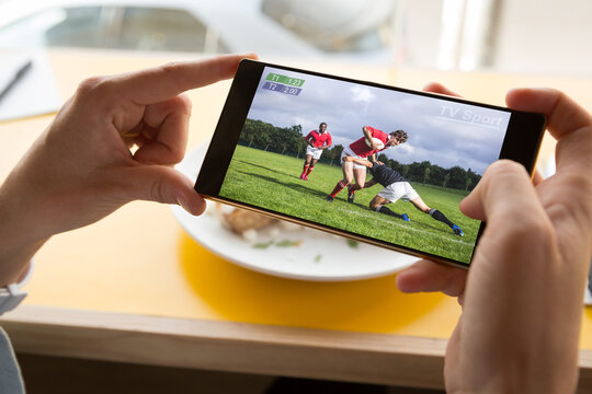 Hands of caucasian man at restaurant watching rugby match on smartphone
