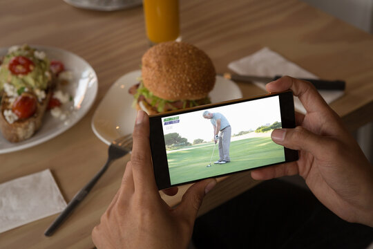 Hands of african american man at restaurant watching golf on smartphone