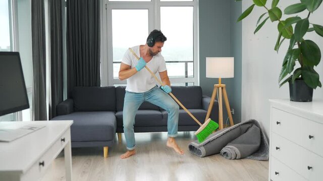 Man listens to music with headphones and cleaning the house and having fun dancing with a broom