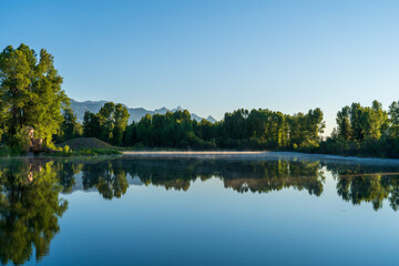 Just after sunrise on a summer day, the Teton mountains reflect on a lake with crystal clear water