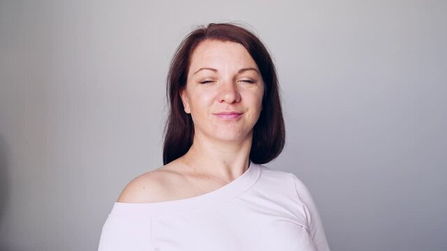 Young woman portrait. Pretty bussiness face. Lifestyle happy emotions. White t-shirt. Looking at camera. Grey background. Copyspace. Adult people. Closed eyes