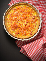 Top view of Uncut traditional French pie quiche Lorraine with bacon, onion and chicken eggs. Backed custard dough served on rustic kitchen towel. Classic recipe. German pie. Black background.

